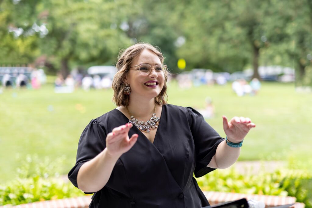 Sandra wears a black top and conducts while smiling